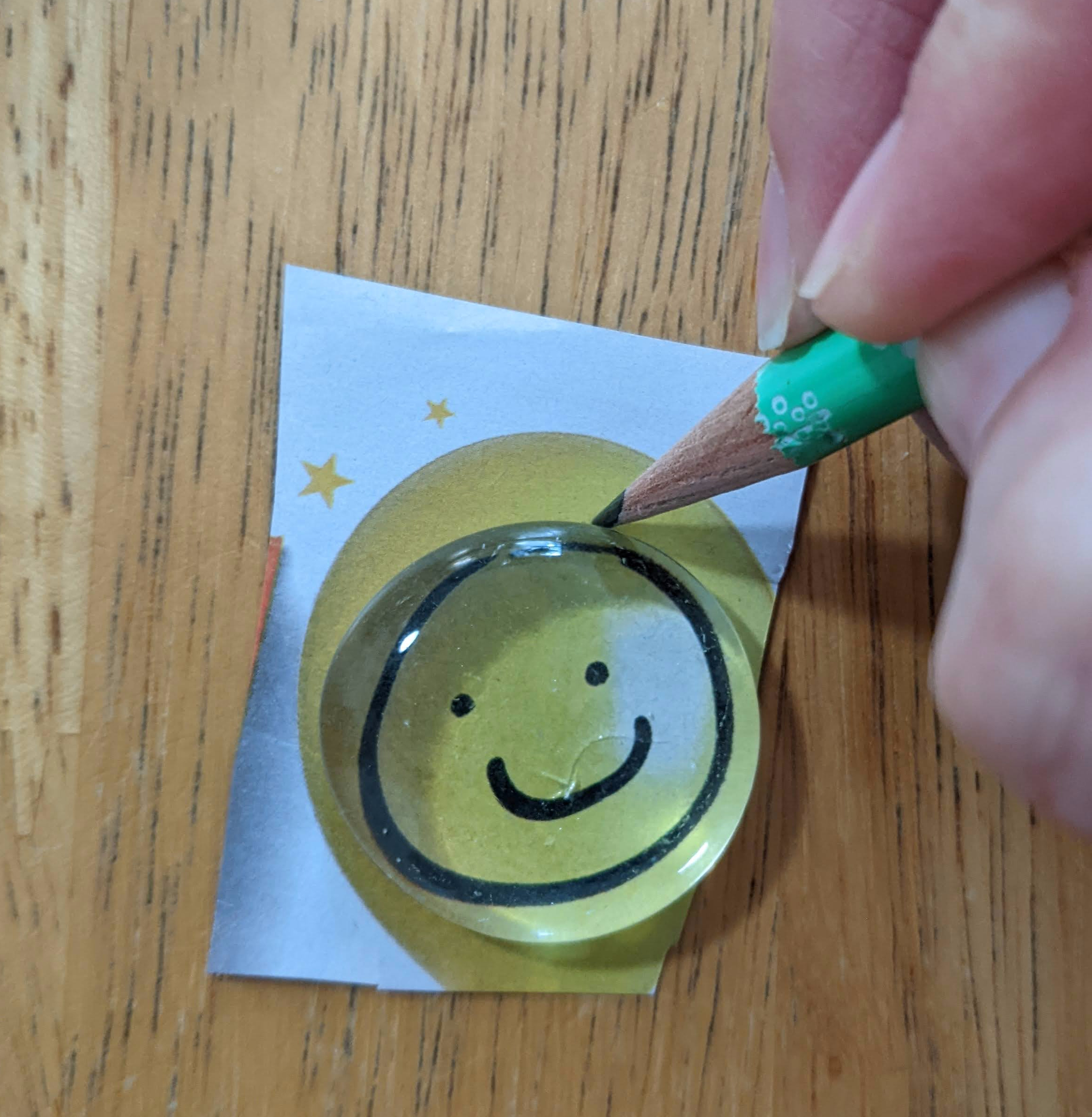 photo of a pencil held by white hands tracing around a picture using a glass gem